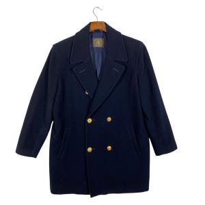 May include: A navy blue double-breasted coat with gold-colored buttons. The coat has a classic design with a notched collar and two front pockets. The coat is hanging on a wooden hanger.