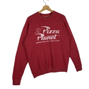 Puede incluir: Sudadera roja con un gr&aacute;fico blanco del logotipo de Pizza Planet y el texto "Serving your local star cluster".