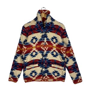 May include: A long-sleeve knit cardigan featuring a shawl collar and a repeating geometric pattern in cream, red, blue, and yellow. The front closure consists of four silver-toned metal buttons, and the garment includes two front pockets.