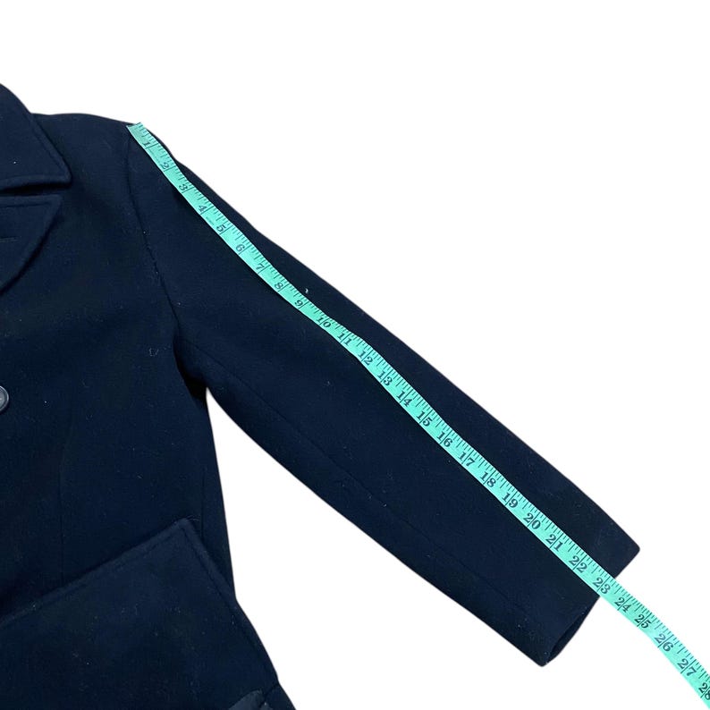 Pu&ograve; includere: Un cappotto nero in lana con un design doppiopetto. Un metro a nastro mostra che la lunghezza della manica &egrave; di circa 71 cm. Il cappotto ha un risvolto a lancia e una tasca con patta. Il cappotto &egrave; fotografato su sfondo bianco.