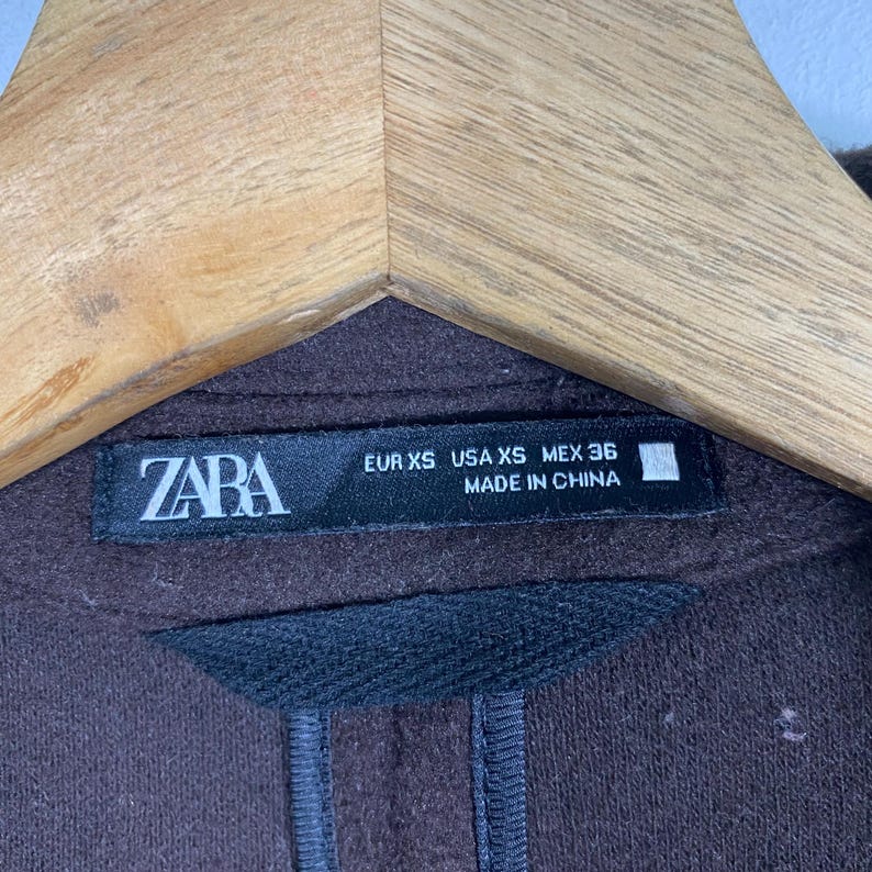 Pu&ograve; includere: Un maglione marrone Zara con un'etichetta nera che recita "ZARA EUR XS USA XS MEX 36 MADE IN CHINA".