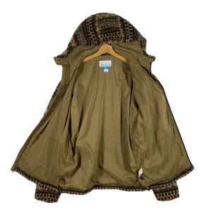 Puede incluir: Una chaqueta de forro polar con estampado marr&oacute;n y beige, con cierre de cremallera y capucha. La chaqueta est&aacute; abierta y el forro es de color marr&oacute;n s&oacute;lido. La chaqueta tiene un logotipo de Columbia en el interior.