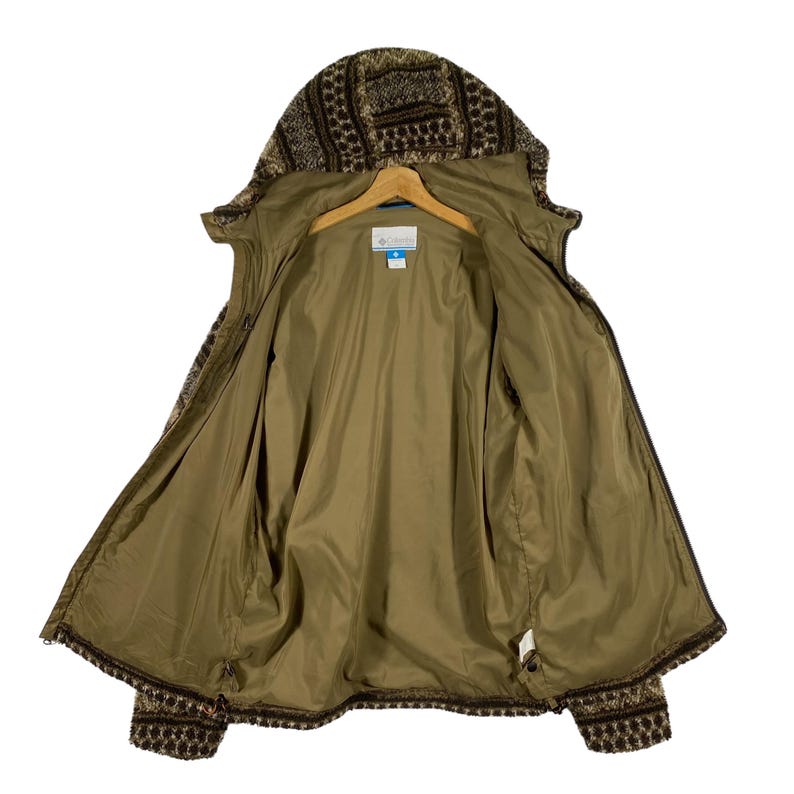 Puede incluir: Una chaqueta de forro polar con estampado marr&oacute;n y beige, con cierre de cremallera y capucha. La chaqueta est&aacute; abierta y el forro es de color marr&oacute;n s&oacute;lido. La chaqueta tiene un logotipo de Columbia en el interior.