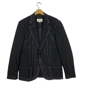 May include: A black blazer with white stitching outlining the seams and pockets. The blazer has a single button closure and a notched lapel.
