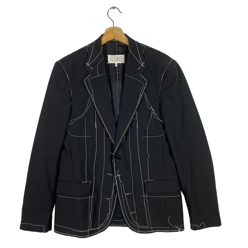 May include: A black blazer with white stitching outlining the seams and pockets. The blazer has a single button closure and a notched lapel.