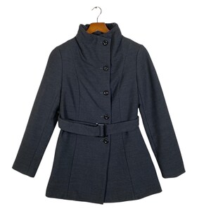 May include: A dark grey coat with a high collar and a matching belt. The coat has a button-up front and is hanging on a wooden hanger. The coat's design is tailored, with a fitted waist and flared hem.