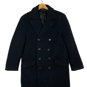 Pu&ograve; includere: Una tazza di ceramica bianca con manico nero e la scritta "But First, Coffee" in stile scritto a mano. La tazza &egrave; su una superficie bianca. La tazza &egrave; alta 10 cm.