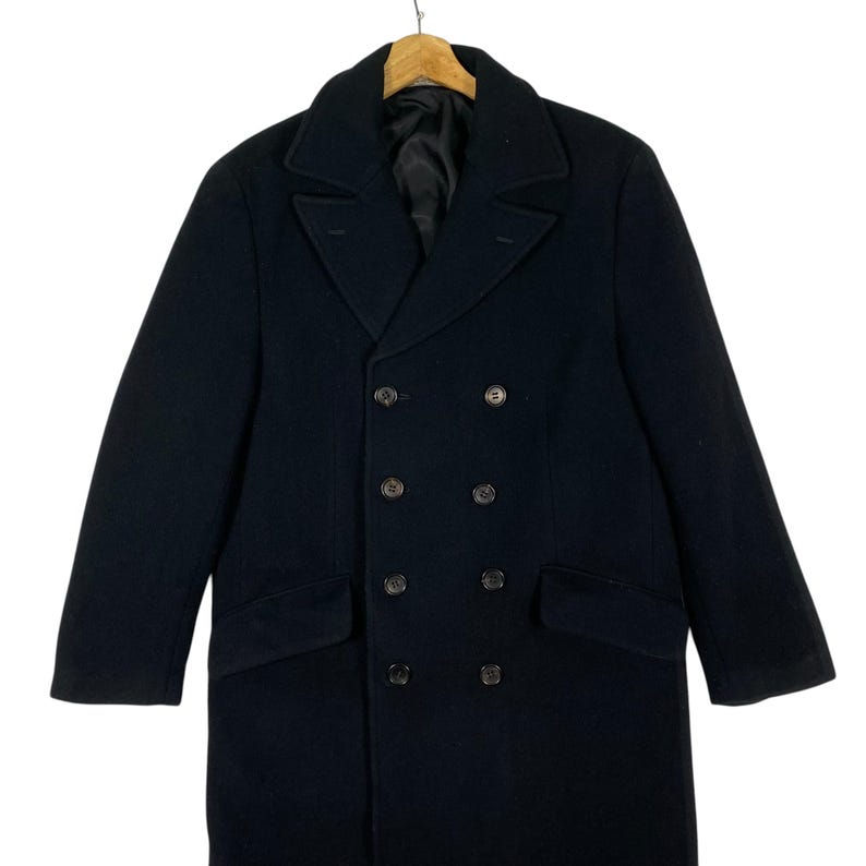 Pu&ograve; includere: Una tazza di ceramica bianca con manico nero e la scritta "But First, Coffee" in stile scritto a mano. La tazza &egrave; su una superficie bianca. La tazza &egrave; alta 10 cm.