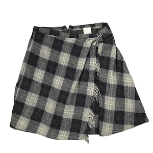 Puede incluir: Una falda de cuadros negros y blancos con un dobladillo deshilachado. La falda está hecha de una tela gruesa y tejida y tiene un estilo de envoltura.