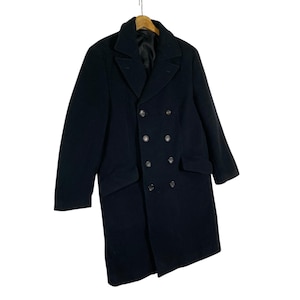 Pu&ograve; includere: Un cappotto nero doppiopetto dal design classico. Il cappotto presenta un colletto a revers, due tasche anteriori e diversi bottoni. Il cappotto &egrave; appeso a una gruccia di legno.