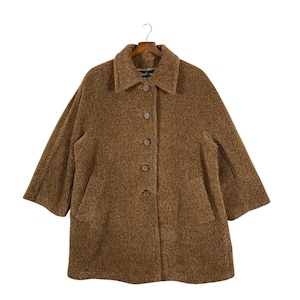 May include: A brown, textured coat with a collared neckline and three-quarter sleeves. The coat features a button-down closure and two front pockets. The coat is hanging on a wooden hanger against a white background.