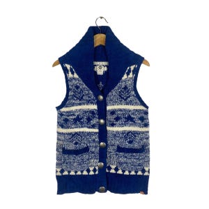 May include: A blue and white patterned knitted waistcoat with a wide collar and button fastening. The waistcoat has two pockets on the front.
