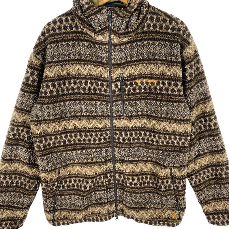 Puede incluir: Una chaqueta de forro polar con estampado marr&oacute;n y beige con cierre de cremallera completo. La chaqueta tiene un cuello alto y un bolsillo con cremallera en el lado izquierdo.