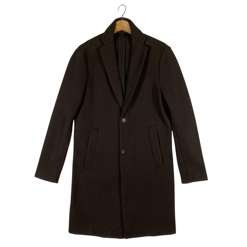 Pu&ograve; includere: Un cappotto lungo a maniche lunghe di colore marrone scuro con una chiusura a bottone singolo e due tasche. Il cappotto ha una vestibilit&agrave; classica e sartoriale.