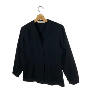 Puede incluir: Una chaqueta negra de botones con cuello y mangas largas. La etiqueta "Comme des Gar&ccedil;ons" es visible en el cuello.