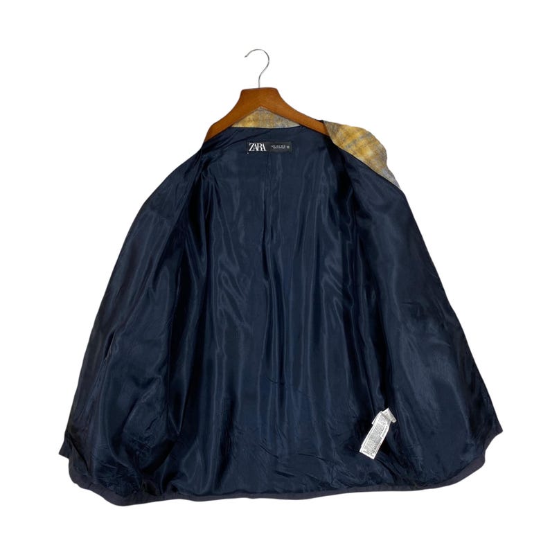 May include: A blazer with a yellow and gray patterned exterior and a navy blue interior. The jacket is hanging on a wooden hanger. The interior lining is a solid navy blue color. The brand tag is visible.