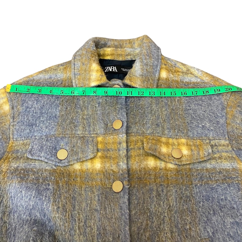May include: A gray and yellow plaid jacket with gold buttons and two chest pockets. The jacket has a collar and is labeled "ZARA". The jacket measures approximately 20 inches across the top.