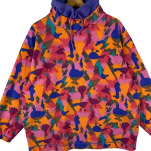 May include: A vintage fleece pullover with a colorful geometric pattern featuring abstract birds and triangles. The fleece is orange, pink, purple, blue, and green. The pullover has a high neck and a purple lining.