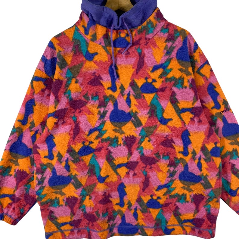 May include: A vintage fleece pullover with a colorful geometric pattern featuring abstract birds and triangles. The fleece is orange, pink, purple, blue, and green. The pullover has a high neck and a purple lining.