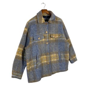 May include: A blue and yellow plaid jacket with a button-up front and two chest pockets. The jacket is made of a soft, fuzzy material and hangs on a wooden hanger.
