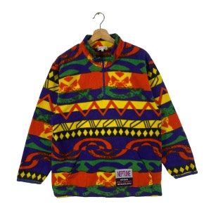 Puede incluir: Un jersey de forro polar colorido con un patr&oacute;n geom&eacute;trico en tonos de rojo, amarillo, verde, azul y negro. El jersey tiene una cremallera y un peque&ntilde;o parche con el texto "NEPTUNE" y "ADVENTURES EXPRESS" en la parte delantera.