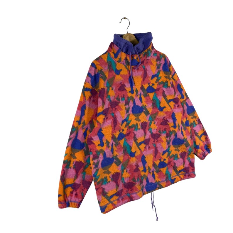 May include: A colorful fleece pullover with a high neck and a drawstring at the bottom. The fleece is patterned with abstract shapes and birds in shades of orange, pink, blue, and green.