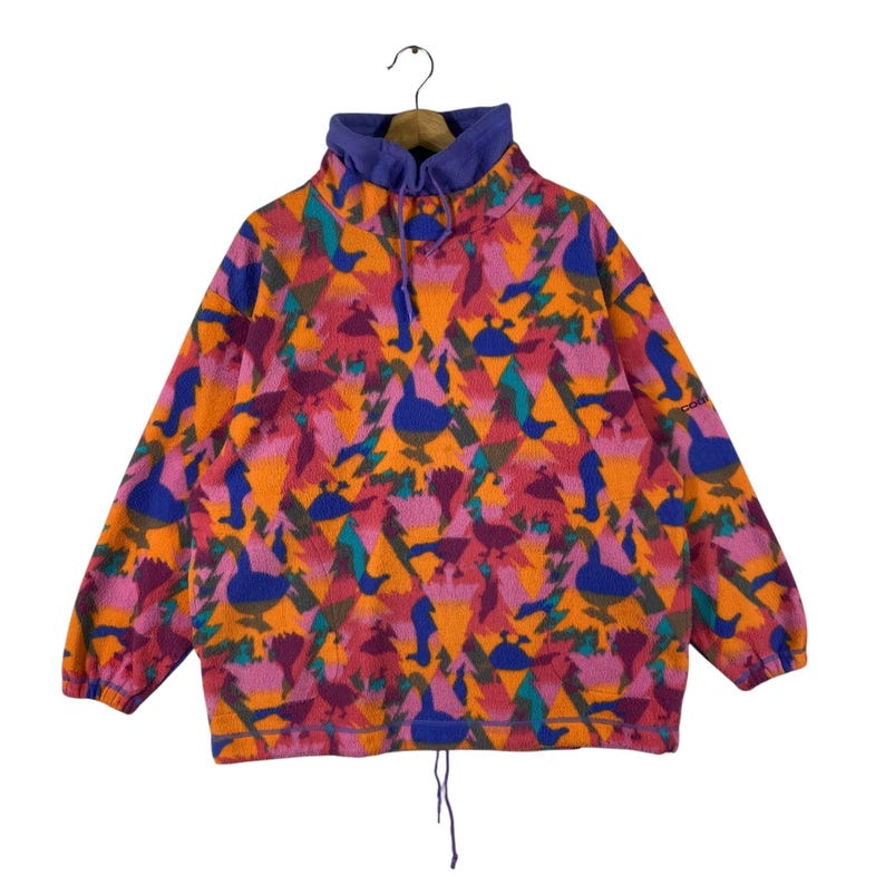 May include: A colorful fleece pullover with a geometric pattern featuring birds and trees. The pullover has a high neck and a drawstring at the neck.