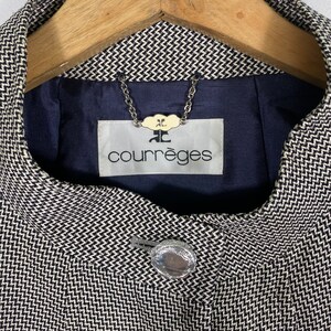 Puede incluir: Una chaqueta con estampado en blanco y negro con un bot&oacute;n plateado y una etiqueta que dice "Courr&egrave;ges" con un peque&ntilde;o logotipo encima del texto.