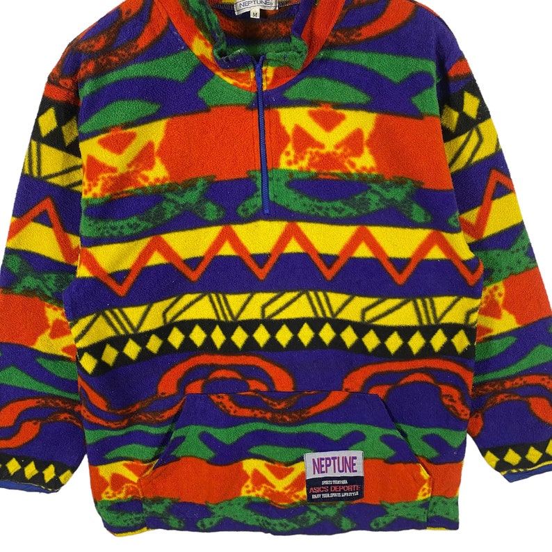 Puede incluir: Un jersey de forro polar colorido con un patr&oacute;n geom&eacute;trico en tonos de rojo, amarillo, verde, azul y negro. El jersey tiene una cremallera de media cremallera y un bolsillo canguro. La etiqueta dice "Neptune Sportswear ASICS Deporte Play Your Game Lifestyle".