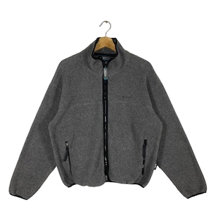 Puede incluir: Chaqueta polar gris con cremallera negra completa y dos bolsillos laterales. La chaqueta tiene cuello alto y ribetes negros. El nombre de la marca está bordado en el pecho.