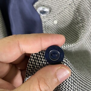 Puede incluir: Primer plano de una tela con estampado en blanco y negro con un bot&oacute;n azul que dice "Courreges" en un dise&ntilde;o circular.
