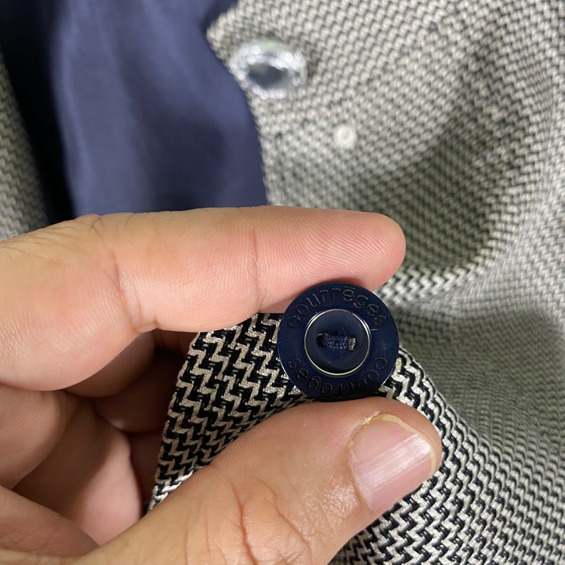 Puede incluir: Primer plano de una tela con estampado en blanco y negro con un bot&oacute;n azul que dice "Courreges" en un dise&ntilde;o circular.