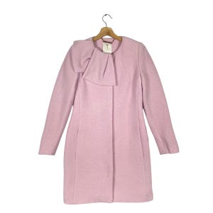 May include: A pink wool coat with a large bow at the neckline. The coat has long sleeves and a button closure.