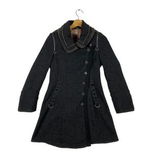 May include: A dark grey wool coat with a large collar and a button fastening. The coat has a unique asymmetrical design with a longer hem at the back. The collar is trimmed with a brown leather-like material and has a decorative metal buckle.