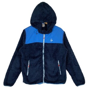 Puede incluir: Una chaqueta de forro polar azul y azul claro con capucha y cierre de cremallera. La chaqueta tiene un pequeño logotipo en el pecho que dice "Igloo" con un gráfico de pingüino.