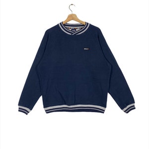 May include: A navy blue sweatshirt with a white and gray striped collar and cuffs. The sweatshirt has a small "ellesse" logo on the front.
