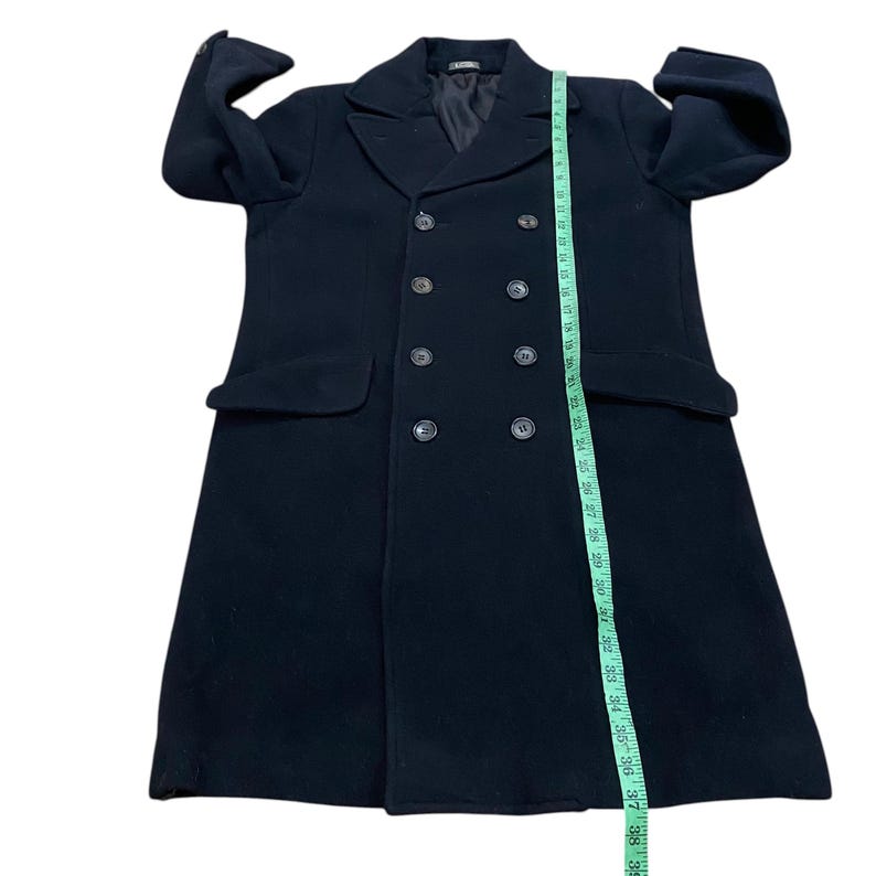 Pu&ograve; includere: Un cappotto nero doppiopetto con sei bottoni e due tasche anteriori. Un metro a nastro mostra la lunghezza del cappotto in centimetri. Il cappotto ha un design classico e su misura.