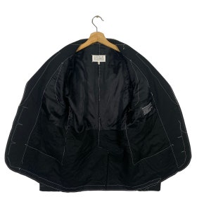 May include: Black blazer with white stitching detail. The inside of the blazer is lined with black fabric. The label reads "Maison Margiela" in white text.