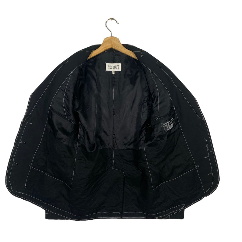 May include: Black blazer with white stitching detail. The inside of the blazer is lined with black fabric. The label reads "Maison Margiela" in white text.