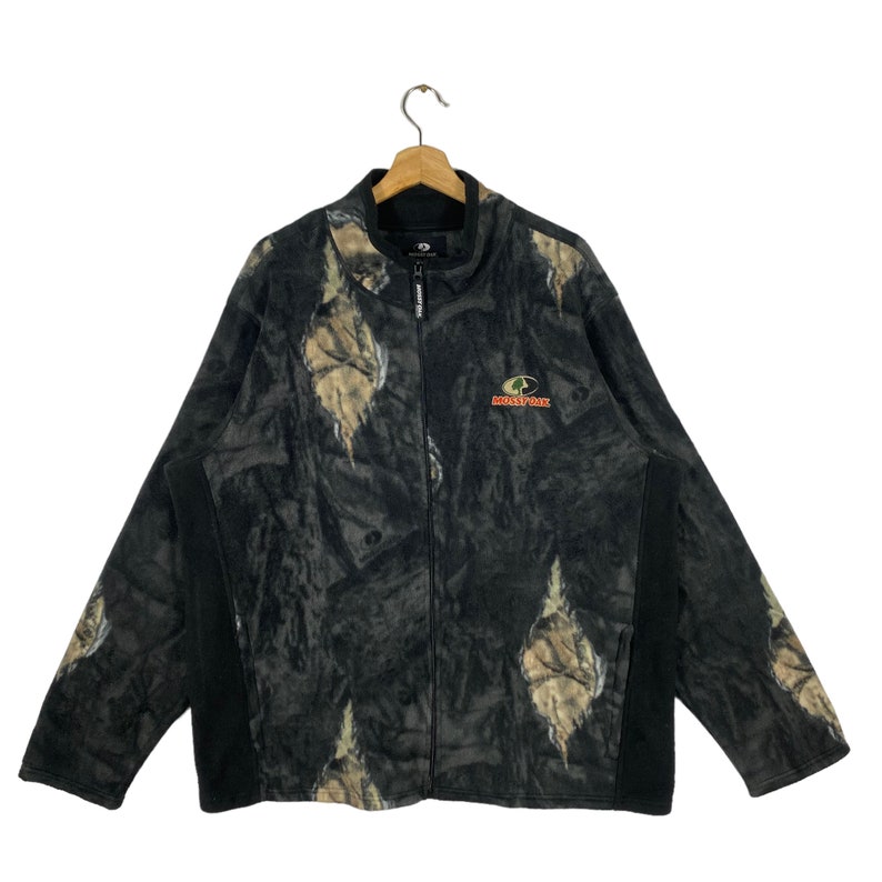 May include: A black and green camouflage fleece jacket with a black zipper and a red and black "MOOSEY OAK" logo on the front.