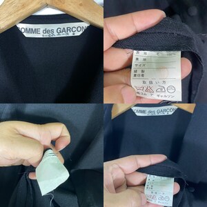 Puede incluir: Camisa negra de manga larga con una etiqueta blanca que dice "COMME des GARCON" y una etiqueta de cuidado blanca con instrucciones en japon&eacute;s.