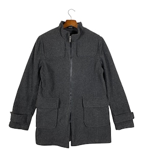 May include: A charcoal gray wool coat with a full-length zipper, two front pockets, and a stand-up collar. The coat has long sleeves with buttoned cuffs and is hanging on a wooden hanger.
