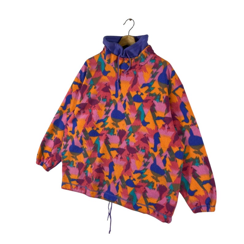 May include: A vintage fleece pullover with a colorful geometric pattern featuring ducks and trees. The fleece is a bright pink, orange, blue, and green. The pullover has a high neck and a drawstring at the bottom.