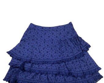 Peut inclure: Une jupe bleue à volants superposés. La jupe est recouverte d'un motif de petits crânes.