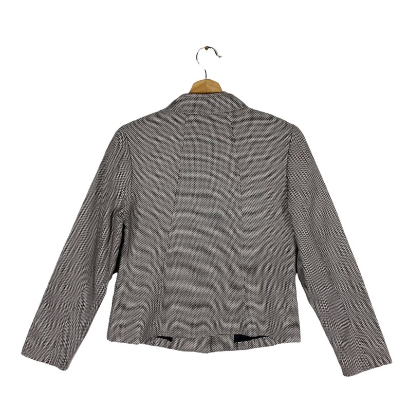 Puede incluir: Una chaqueta de traje de patr&oacute;n blanco y negro con cuello de muesca y mangas largas. La chaqueta est&aacute; colgada en una percha de madera.