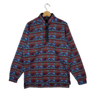 May include: A blue, red, and green patterned fleece pullover with a 1/4 zip closure. The zipper has a black pull tab and the brand name "Fleece" is embroidered in red on the collar.