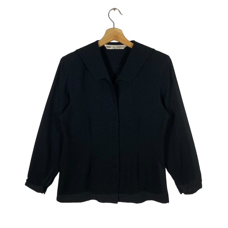 Puede incluir: Una camisa negra de manga larga con botones, cuello grande y una etiqueta que dice "Comme des Gar&ccedil;ons".