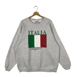 以下が含まれることがあります： 前面にヴィンテージのイタリア国旗のデザインと「ITALIA il bel paese」の文字がプリントされたグレーのスウェットシャツです。