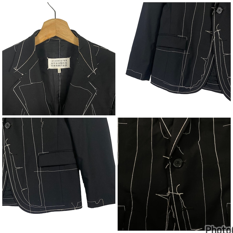 May include: A black blazer with white stitching details. The blazer has a notched lapel, two flap pockets, and a single button closure. The label on the inside of the blazer reads "0123456789 10 11 12 13 14 15 16 17 18 19 20 21 22 23"