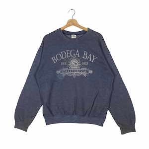 Könnte beinhalten: Ein blaues Sweatshirt mit einem weißen Grafikdruck, auf dem "Bodega Bay Est. 1852 California" steht.